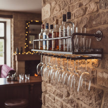 Load image into Gallery viewer, Industrial metal wine shelf with bottles above and hanging wine glasses below on a stone wall