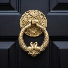 Load image into Gallery viewer, Peacock cast metal door knocker with an antique brass finish on a dark front door