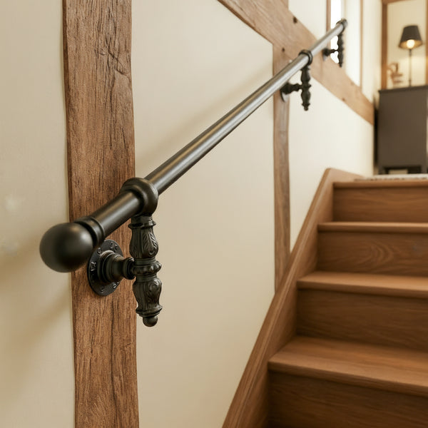 Ornate black stair handrail with decorative drop brackets, circular wall plates and a ball end cap