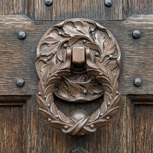Load image into Gallery viewer, Laurel wreath cast metal door knocker with an aged bronze finish on a wooden front door
