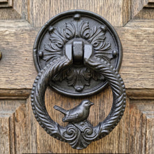Load image into Gallery viewer, Black cast metal bird door knocker with a textured ring, mounted on a rustic wooden door
